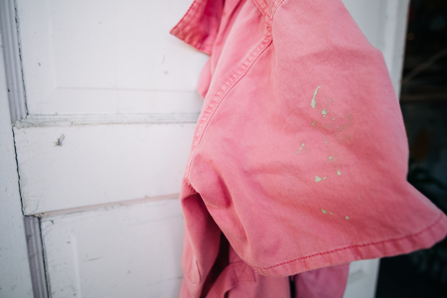 Pink coveralls with speckles of green paint hang on the back of the studio door